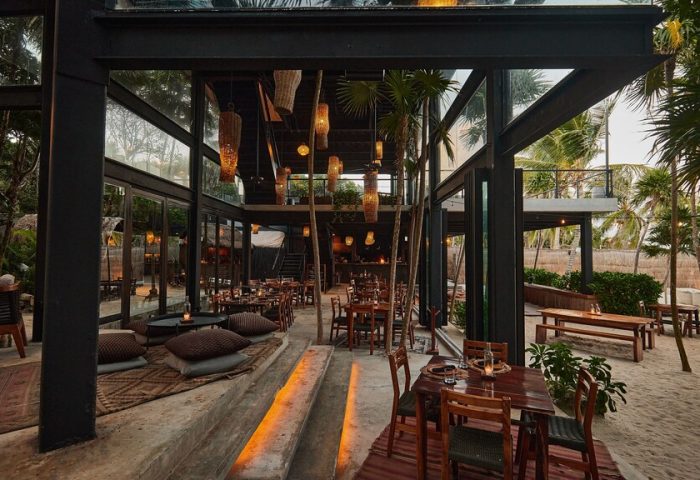 Our Habitas Tulum gay-friendly hotel dining area. Open-air restaurant with wooden tables, pillows, and woven light fixtures.
