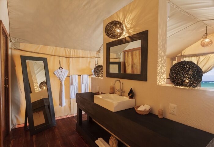 Our Habitas Tulum gay-friendly hotel bathroom. Interior shot of sink, mirror, and lighting in a tented room with a view of the ocean. Luxury gay travel.