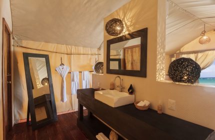 Our Habitas Tulum gay-friendly hotel bathroom. Interior shot of sink, mirror, and lighting in a tented room with a view of the ocean. Luxury gay travel.
