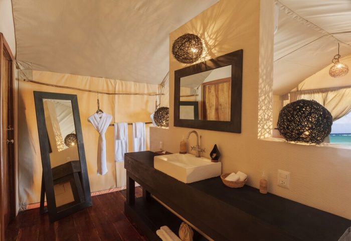 Our Habitas Tulum gay-friendly hotel bathroom. Interior shot of sink, mirror, and lighting in a tented room with a view of the ocean. Luxury gay travel.