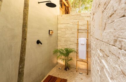 Our Habitas Tulum gay-friendly hotel outdoor shower. Stone walls, wooden ladder with towel, and tropical plant create a natural oasis.