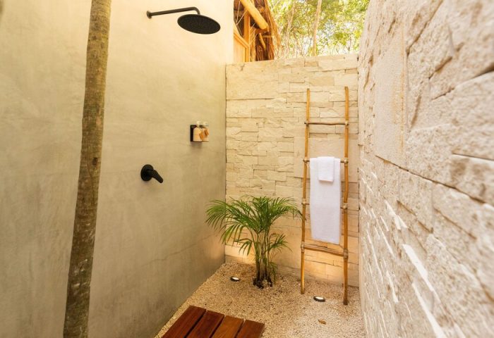 Our Habitas Tulum gay-friendly hotel outdoor shower. Stone walls, wooden ladder with towel, and tropical plant create a natural oasis.