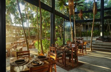 Our Habitas Tulum gay-friendly hotel restaurant. Tables set for dining amidst lush greenery. A serene Tulum travel experience.