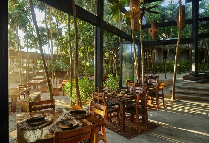 Our Habitas Tulum gay-friendly hotel restaurant. Tables set for dining amidst lush greenery. A serene Tulum travel experience.