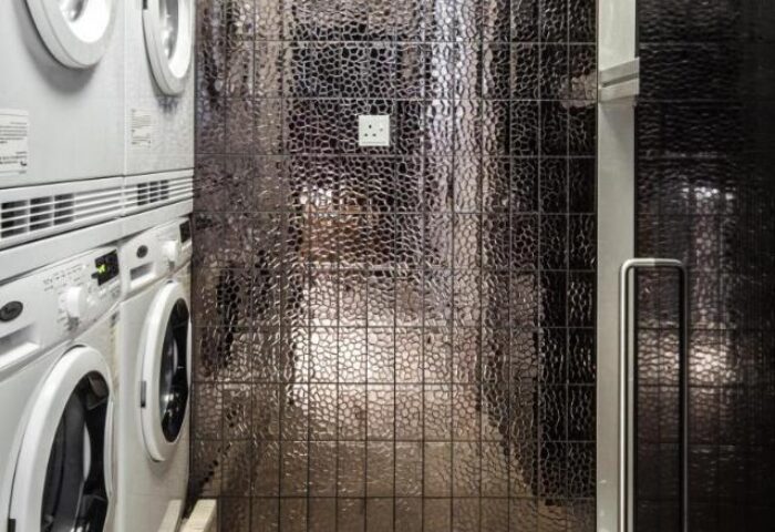 Ovolo Central gay-friendly hotel laundry room. Stacked washing machines next to textured dark tiles. Modern design for gay travelers.