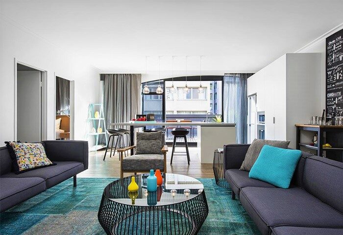 Ovolo Laneways pet-friendly hotel suite: Stylish living area with sofas, coffee table, and kitchen. A gay-friendly hotel for your travel needs.