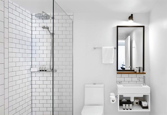 Ovolo Laneways pet-friendly hotel bathroom. White tiled shower, toilet, sink with mirror and toiletries. Gay-friendly hotel design.
