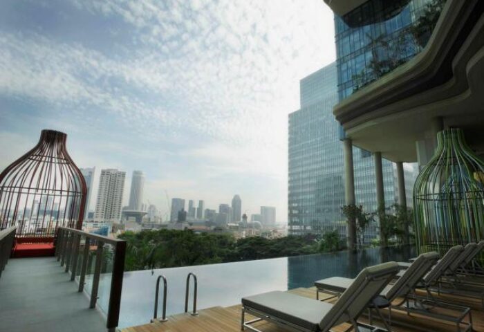 PARKROYAL COLLECTION Pickering Singapore pool. Gay-friendly hotel with city view. Loungers by infinity pool. Singapore skyline.