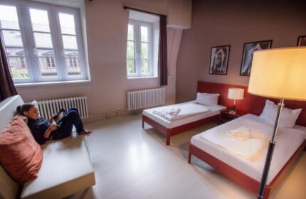 PLUS Berlin Hotel & Hostel: A guest relaxes in a room with twin beds. Gay-friendly lodging option, offering comfort and style for travelers.
