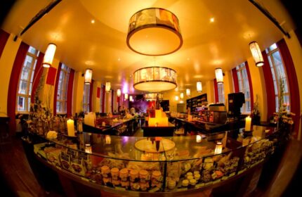 Interior of PLUS Berlin Hotel & Hostel, a gay-friendly hotel. View of the bar area with pastries, warm lighting, and unique hanging lamps.