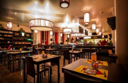 PLUS Berlin Hotel & Hostel's gay-friendly restaurant. Tables are set, and the bar is in the background. Warm lighting creates a welcoming atmosphere.