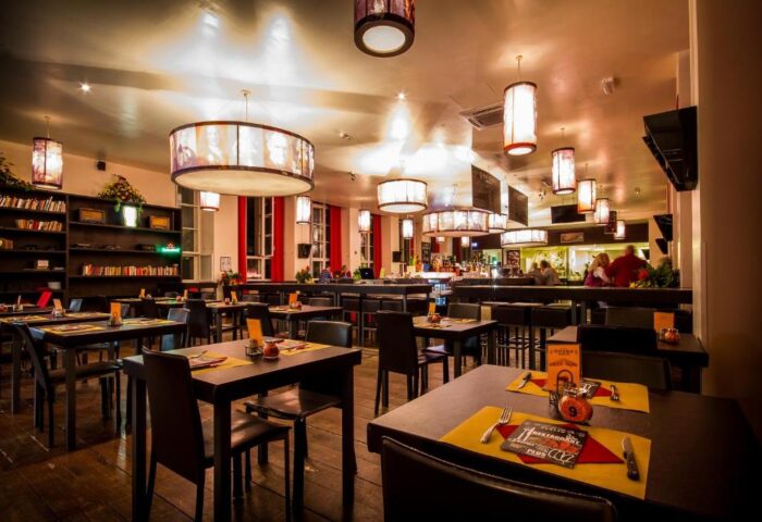 PLUS Berlin Hotel & Hostel's gay-friendly restaurant. Tables are set, and the bar is in the background. Warm lighting creates a welcoming atmosphere.