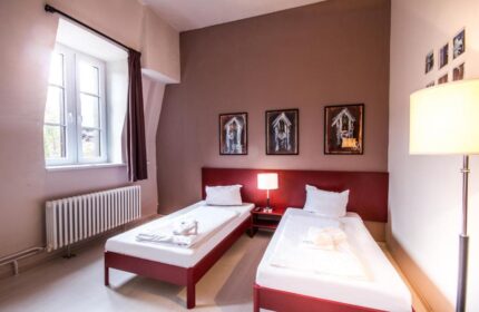 PLUS Berlin Hotel & Hostel room. Gay-friendly hotel with twin beds, red accents, and modern decor. Ideal for gay travelers in Berlin.