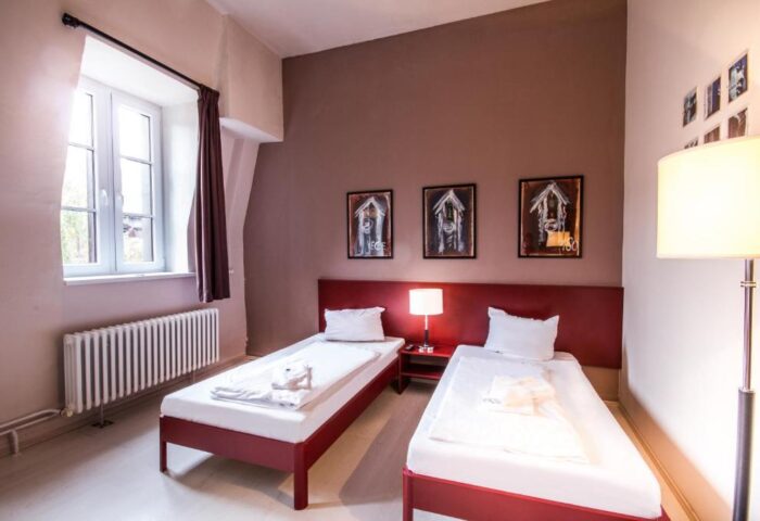 PLUS Berlin Hotel & Hostel room. Gay-friendly hotel with twin beds, red accents, and modern decor. Ideal for gay travelers in Berlin.