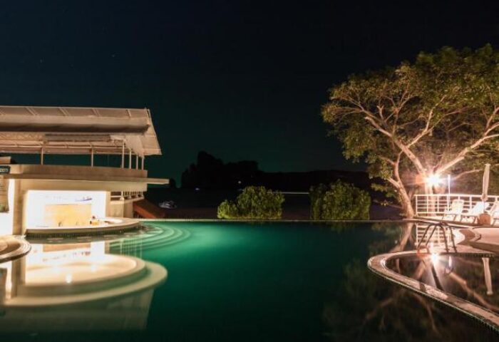 Night view of the pool at PP Charlie Beach Resort, a gay-friendly hotel. Features a bar, trees, and lounge chairs. Perfect for gay travel.