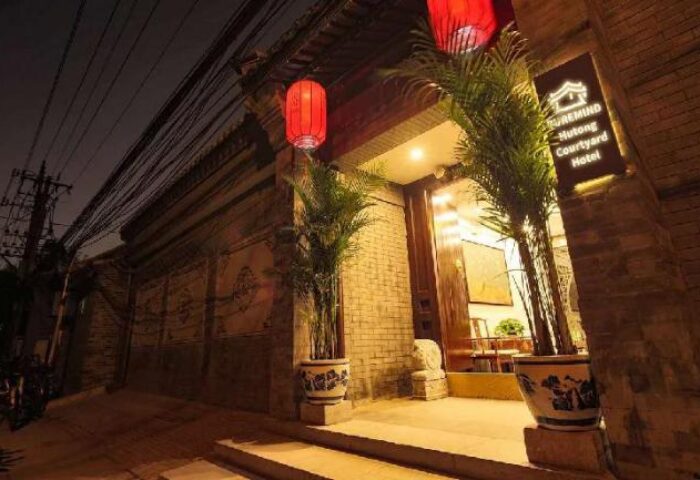 PUREMIND Hutong Courtyard Hotel entrance at night. Gay-friendly hotel with red lanterns, plants, and traditional Chinese architecture.