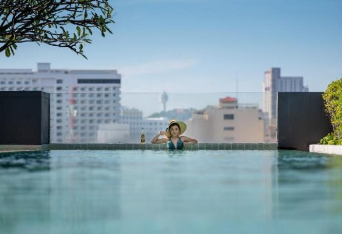 Page 10 Hotel's rooftop pool view. Woman in hat enjoys the infinity pool overlooking the cityscape. Gay-friendly hotel travel.