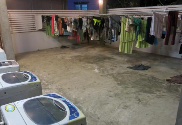 Laundry area at Pak Up Hostel, a gay-friendly hotel. Clothes hang on a line above washing machines. Ideal for gay men travel.