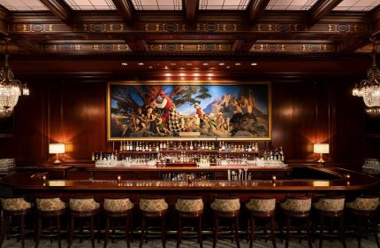 Bar at the gay-friendly Palace Hotel, a Luxury Collection Hotel, San Francisco. Elegant wood paneling, painting, and bar stools. Upscale ambiance.