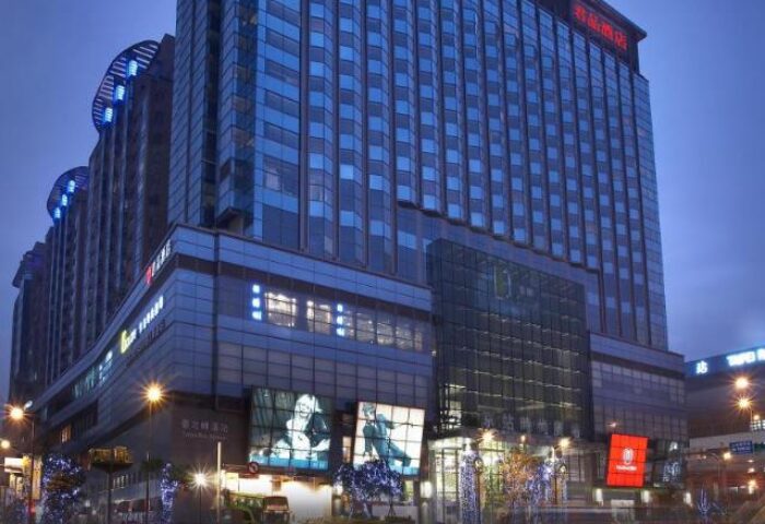 Exterior of Palais de Chine Hotel, a gay-friendly hotel in Taipei. Modern architecture, city lights, and signage visible. Night shot.