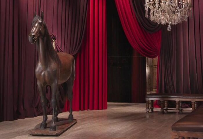 Palais de Chine Hotel interior. Horse statue, red curtains, chandelier, and bench. Gay-friendly hotel decor for discerning travelers.