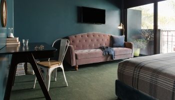 Palihotel Melrose room. Desk, pink sofa, TV, and balcony in a stylish hotel room. Gay-friendly hotel for gay men travel in Los Angeles.