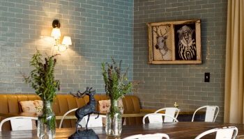 Palihotel Melrose dining area. Gay-friendly hotel interior with a long wooden table, white chairs, and blue brick wall. Stylish design.
