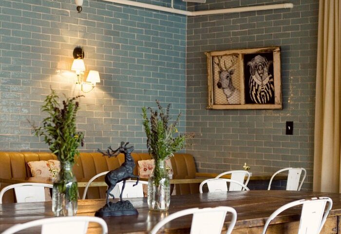 Palihotel Melrose dining area. Gay-friendly hotel interior with a long wooden table, white chairs, and blue brick wall. Stylish design.