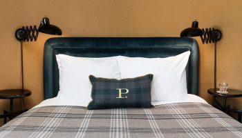 Palihotel Melrose room featuring a bed with a plaid blanket, pillows, headboard, and reading lights. Gay-friendly hotel for gay travel.
