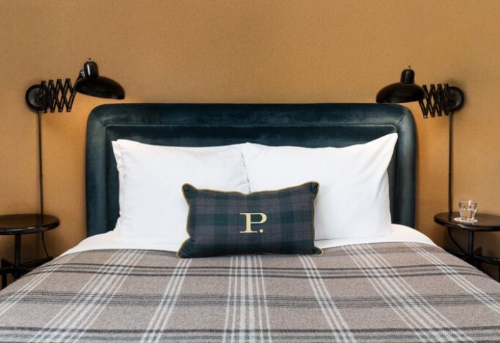 Palihotel Melrose room featuring a bed with a plaid blanket, pillows, headboard, and reading lights. Gay-friendly hotel for gay travel.