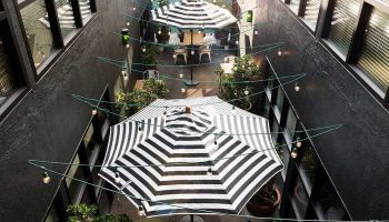 Palihotel Melrose courtyard view. Gay-friendly hotel with striped umbrellas, string lights, and plants. A cool outdoor space for gay travelers.
