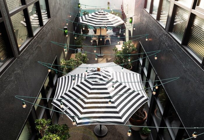 Palihotel Melrose courtyard view. Gay-friendly hotel with striped umbrellas, string lights, and plants. A cool outdoor space for gay travelers.