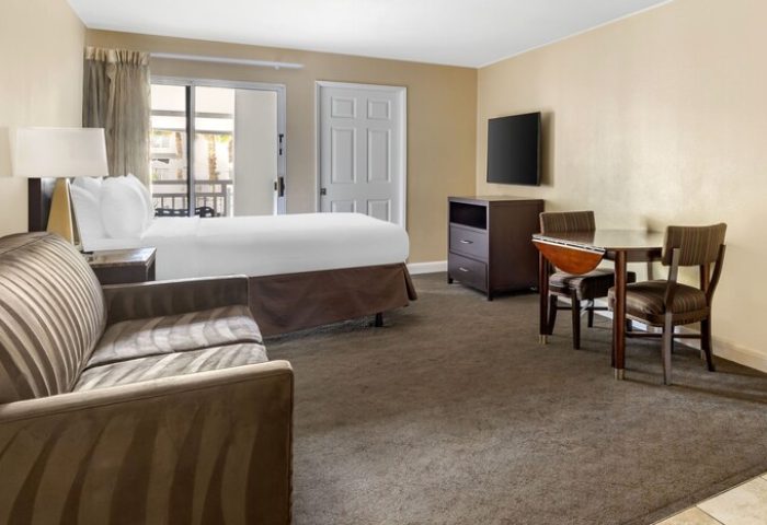 Palm Canyon Resort room. Gay-friendly hotel in Palm Springs features a bed, sofa, dining table, and TV. Perfect for gay men's vacation.