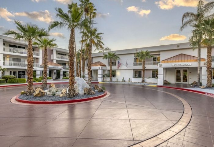 Palm Canyon Resort in Palm Springs, a gay-friendly hotel. The entrance features palm trees and a registration area. Vacation awaits!