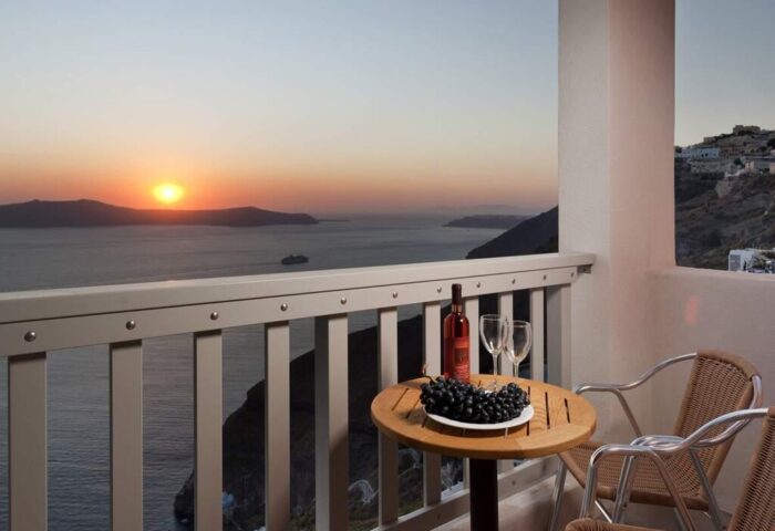 Panorama Boutique Hotel balcony view at sunset. Wine, grapes, and chairs overlook the ocean. Gay-friendly hotel in Santorini.