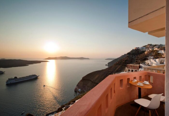 Balcony view at Panorama Boutique Hotel, a gay-friendly hotel. Ocean sunset, cruise ship, table with two cups. Santorini, Greece.