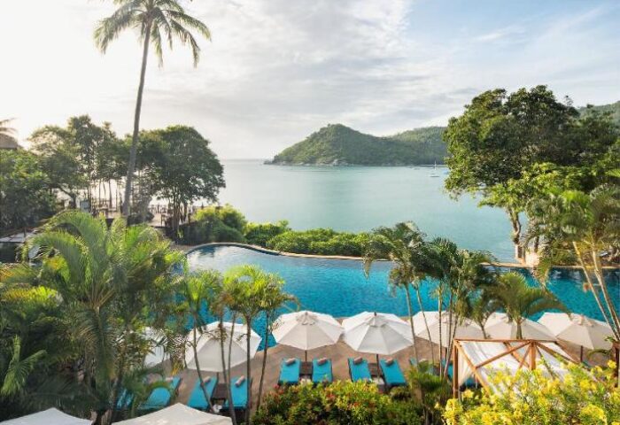 Pool view at Panviman Resort Koh Phangan, a gay-friendly hotel. Tropical paradise with ocean, palm trees, umbrellas, and lounge chairs.
