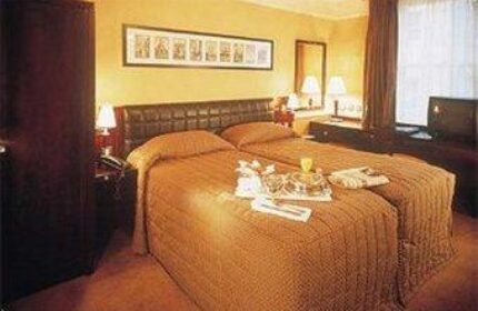 Paramount Hotel room. Gay-friendly hotel with two beds, tray with glasses, TV, and dark furniture. Ideal for gay men's travel.