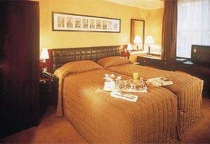Paramount Hotel room. Gay-friendly hotel with two beds, tray with glasses, TV, and dark furniture. Ideal for gay men's travel.