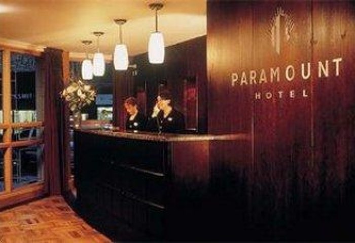Paramount Hotel reception area. Gay-friendly hotel with staff at the front desk. Warm lighting and wood paneling create an inviting atmosphere.