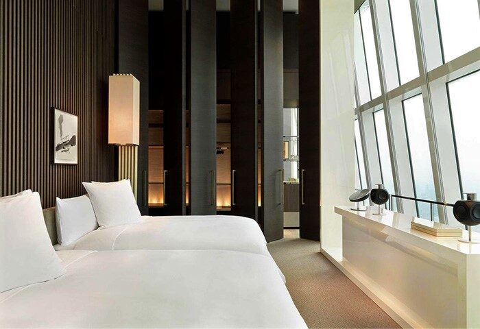 Park Hyatt Shanghai gay-friendly hotel room. Modern interior with twin beds, floor-to-ceiling windows, and dark wood accents. Luxury travel.