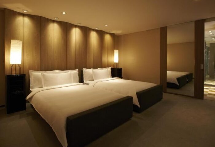 Park Hyatt Tokyo gay-friendly hotel room with two beds. Pet-friendly hotel with modern design and warm lighting. Mirror reflects the room.