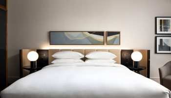 Park Hyatt Toronto gay-friendly hotel room. Modern decor, white linens, and bedside lamps create a welcoming ambiance. Luxury travel.