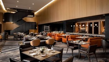 Upscale dining at gay-friendly Park Hyatt Toronto. Restaurant interior with tables, chairs, bar, and staircase. Luxury hotel experience.