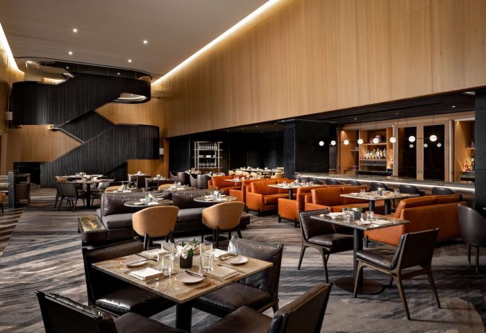 Upscale dining at gay-friendly Park Hyatt Toronto. Restaurant interior with tables, chairs, bar, and staircase. Luxury hotel experience.