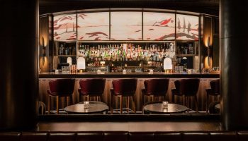 Park Hyatt Toronto's gay-friendly bar. Upscale hotel bar with red leather stools, dark wood, and a backlit mural. Luxury gay travel.