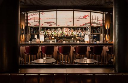 Park Hyatt Toronto's gay-friendly bar. Upscale hotel bar with red leather stools, dark wood, and a backlit mural. Luxury gay travel.
