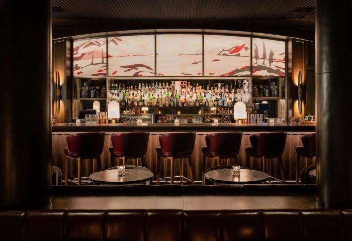Park Hyatt Toronto's gay-friendly bar. Upscale hotel bar with red leather stools, dark wood, and a backlit mural. Luxury gay travel.