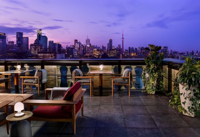 Park Hyatt Toronto's gay-friendly rooftop lounge at dusk. City skyline view, tables, chairs, and plants create an inviting atmosphere.