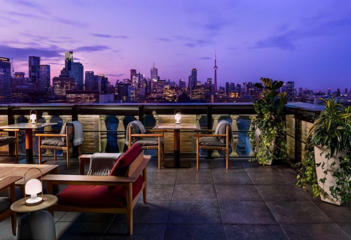 Park Hyatt Toronto's gay-friendly rooftop lounge at dusk. City skyline view, tables, chairs, and plants create an inviting atmosphere.